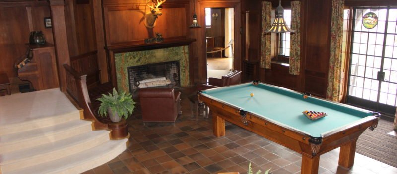 Main hall as of 2020, with pool table as the focal point. Taxidermy deer head is visible over fireplace. Organ console is also visible.