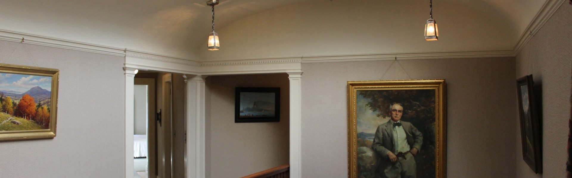 Staircase hall landing facing the guest wing. Tom Plant's portrait hangs near center to the image, Tiffany stained glass ceiling is visible.