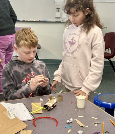 Two students work with recycled materials to build a simple machine