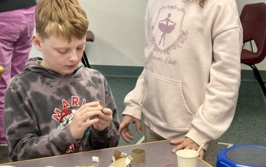 Two students work with recycled materials to build a simple machine